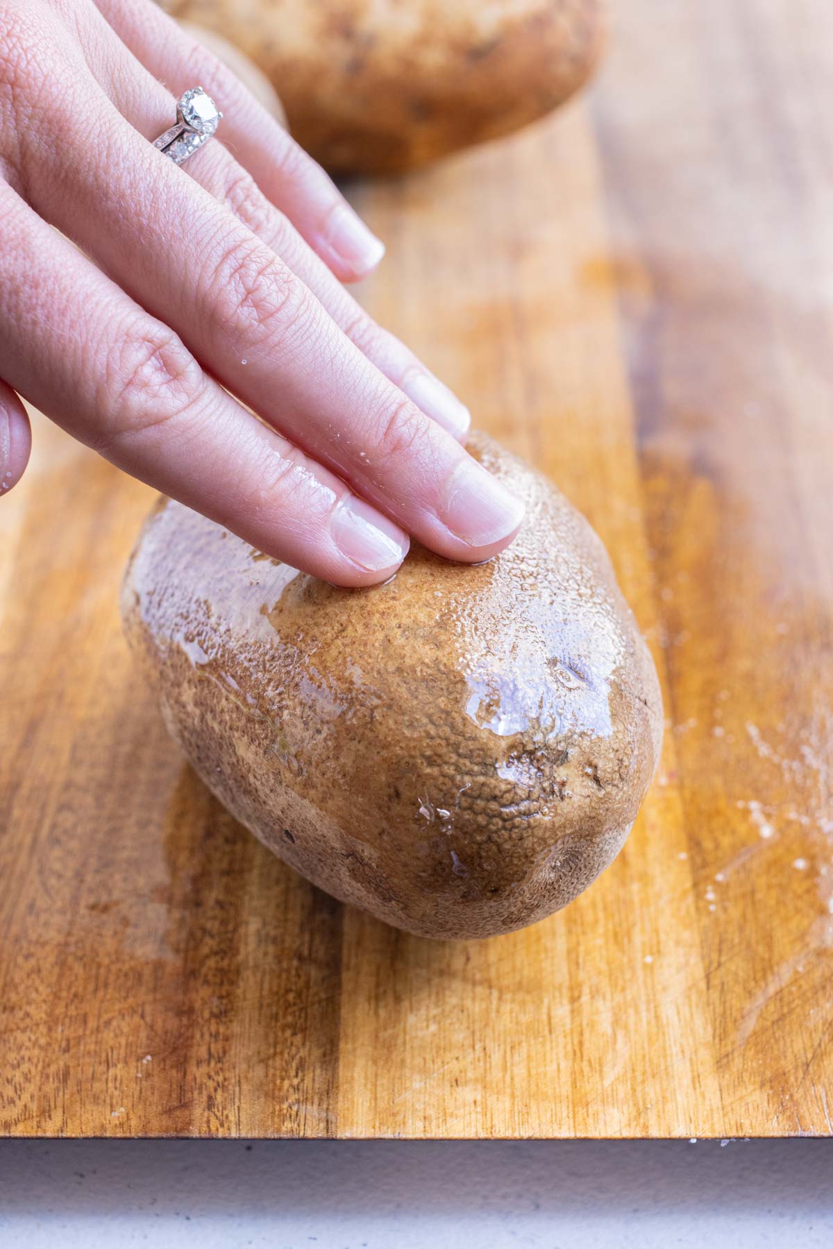 Fingers rub the oil into a potato.