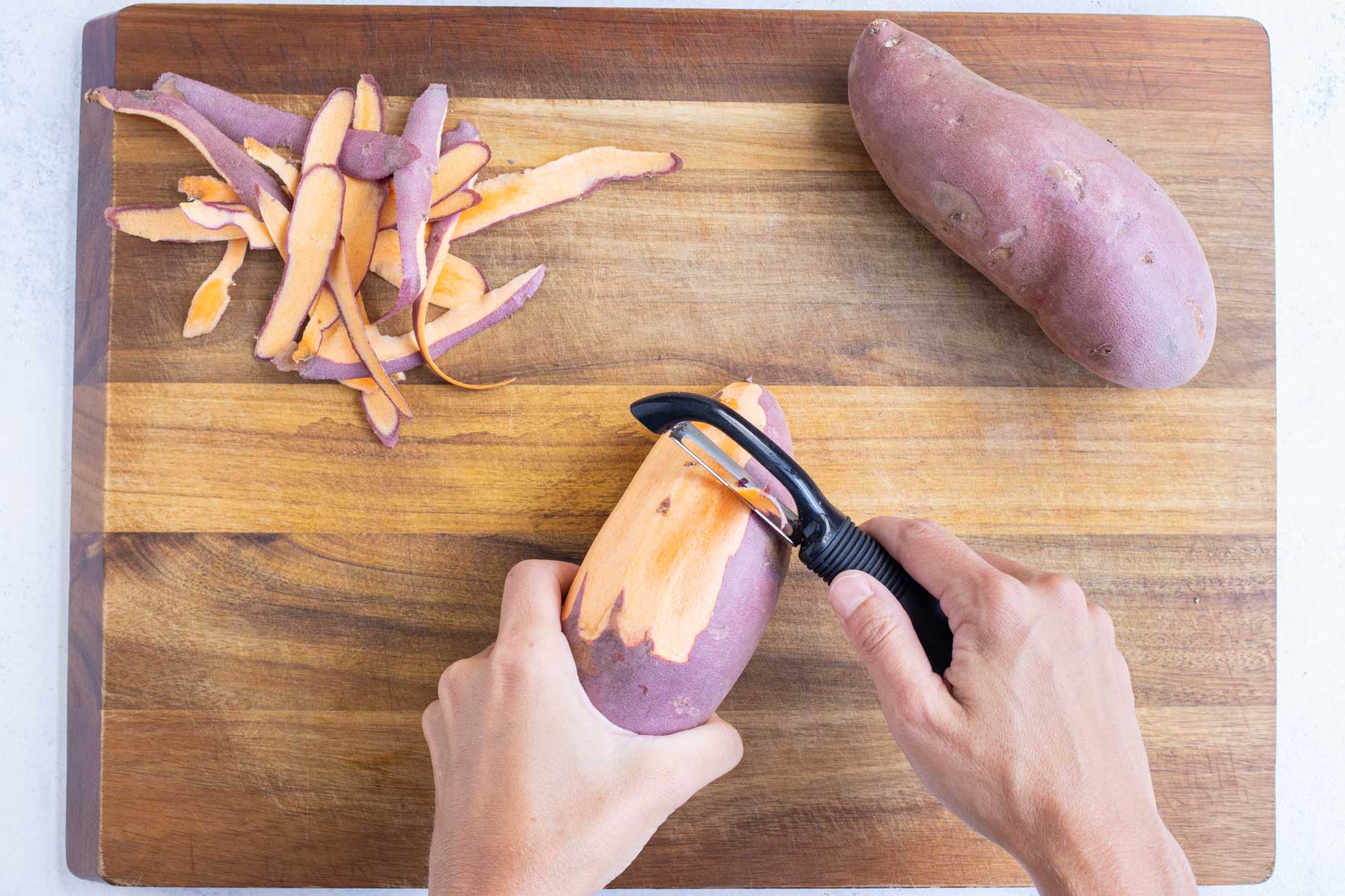 A vegetable peeler removes the skin from a sweet potato.