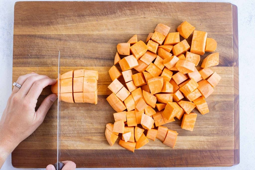 A sharp knife demonstrates how to cut a sweet potato into cubes.