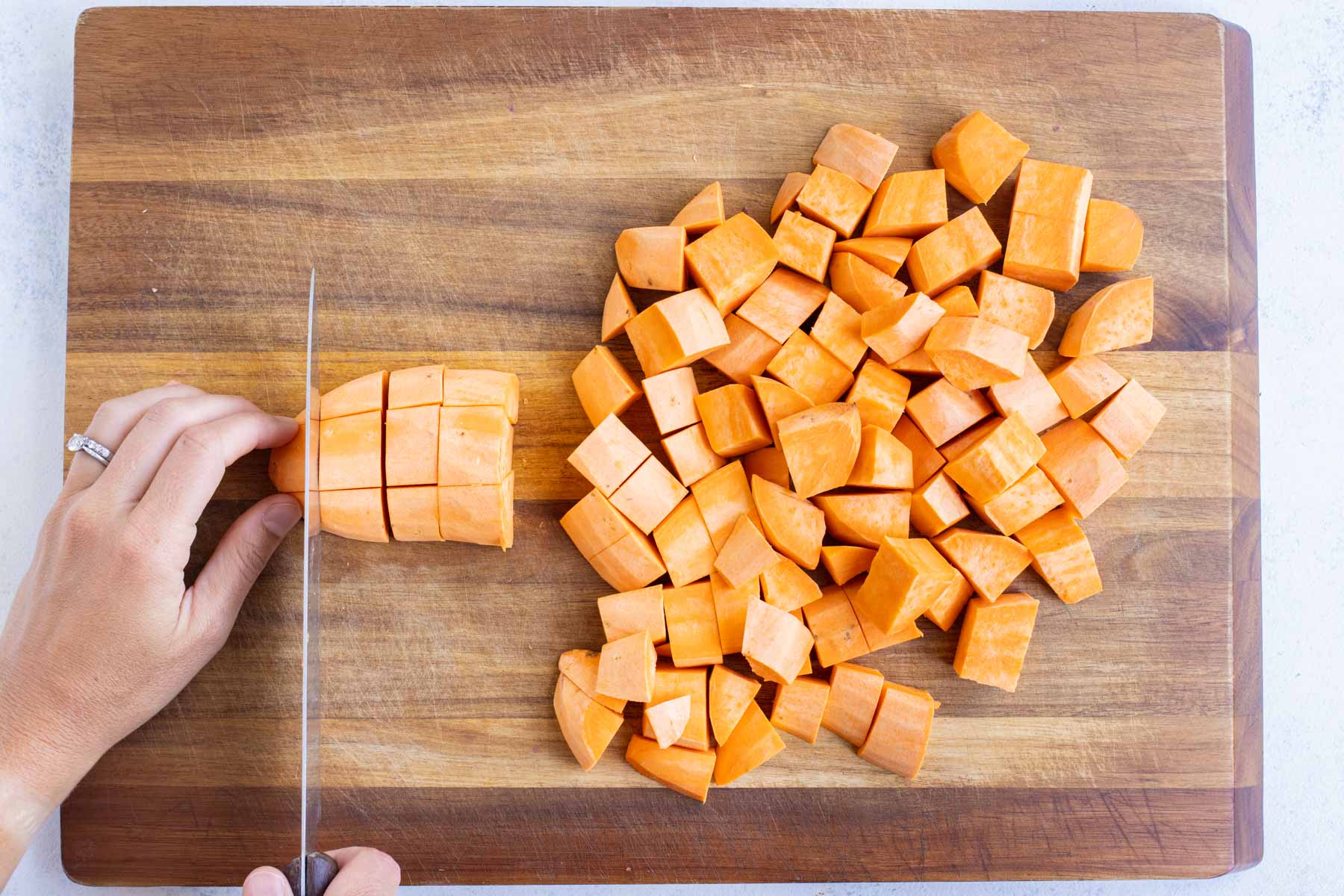 A sharp knife cuts a sweet potato into cubes.