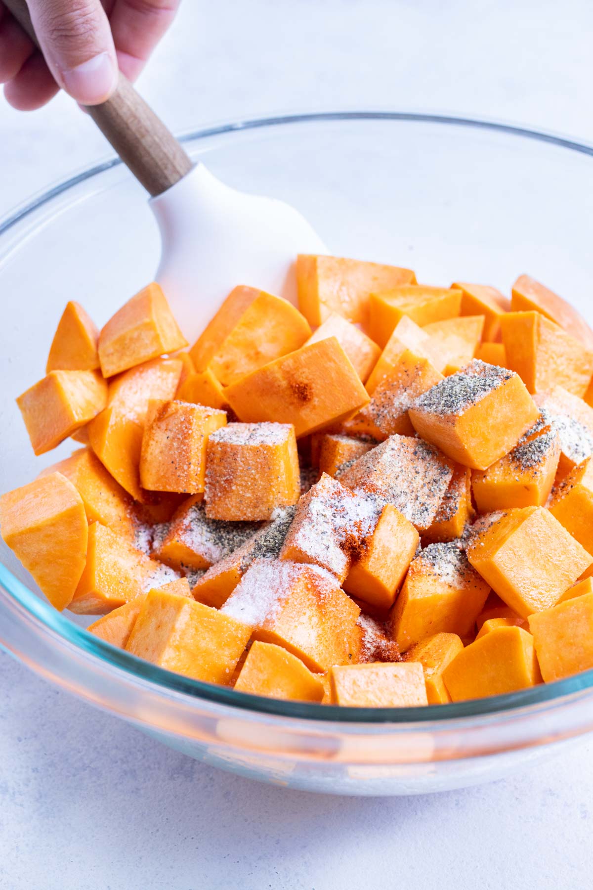 Garlic powder, paprika, salt, and pepper are added to oiled sweet potatoes.