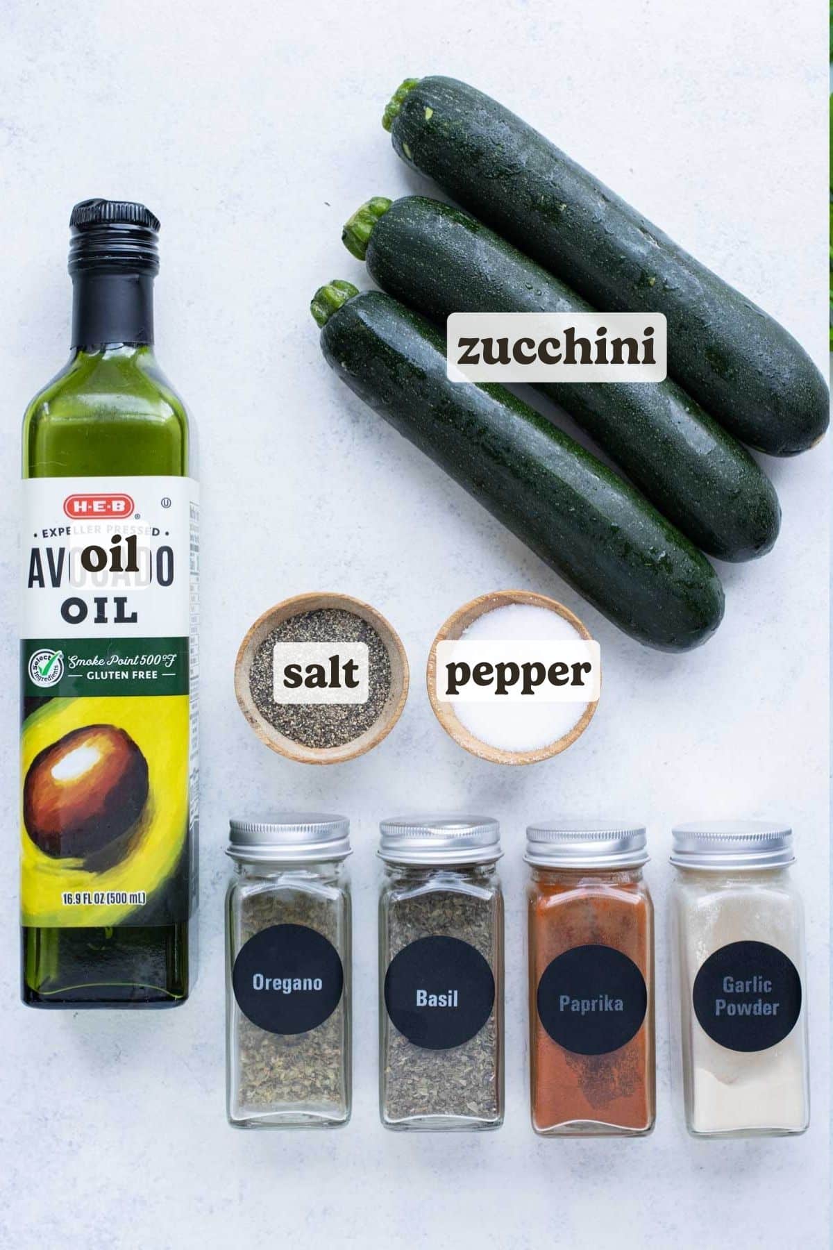 Ingredients for air fryer zucchini including zucchini, oil, garlic powder, dried herbs, and paprika.