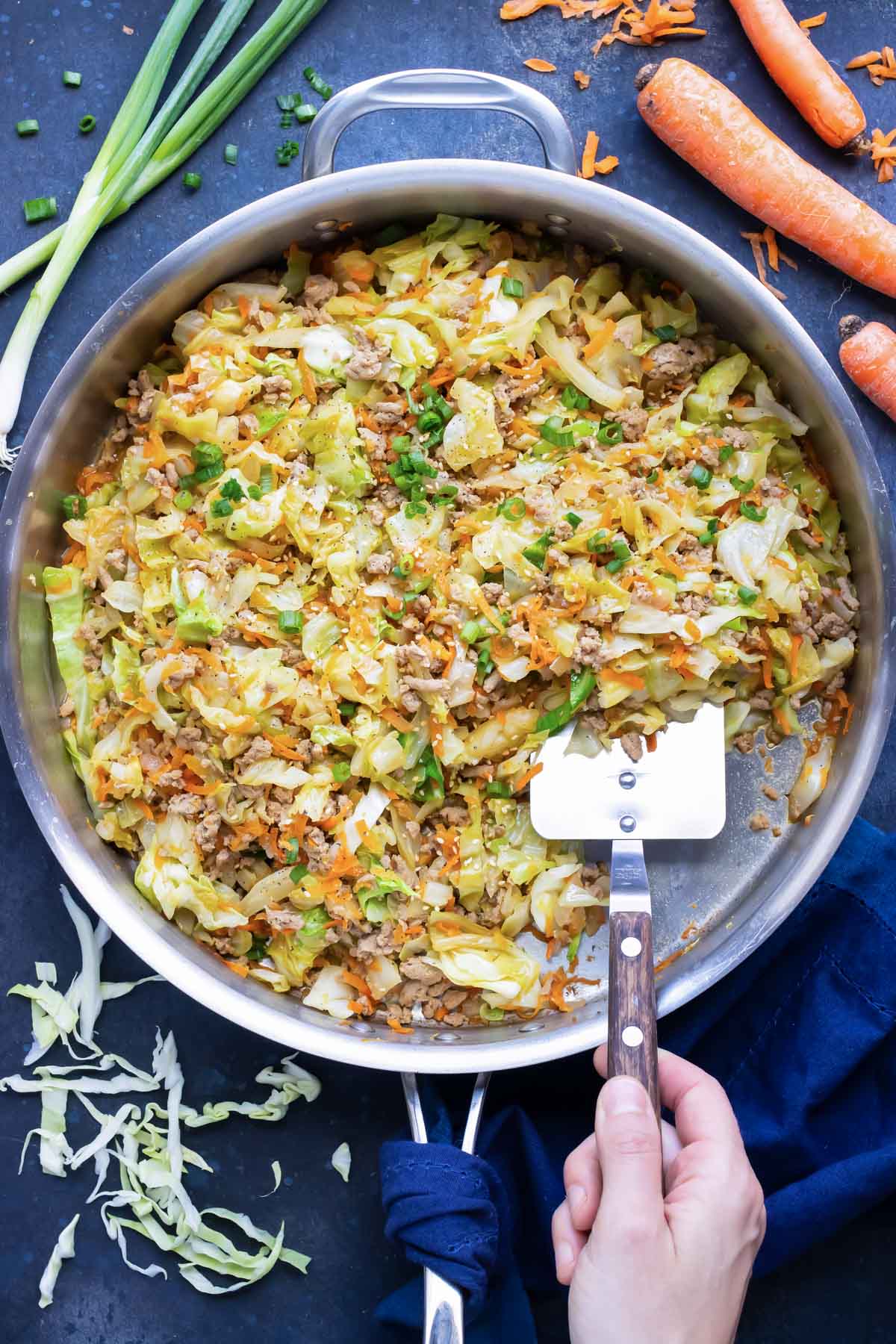 A large skillet full of a Paleo egg roll in a bowl recipe with cabbage, carrots, and ground turkey with a metal spatula scooping out a serving.