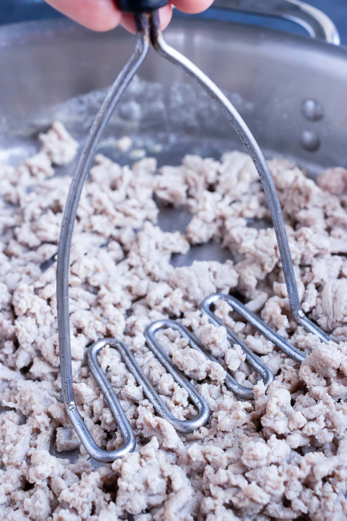 Ground turkey being crumbled with a potato masher.