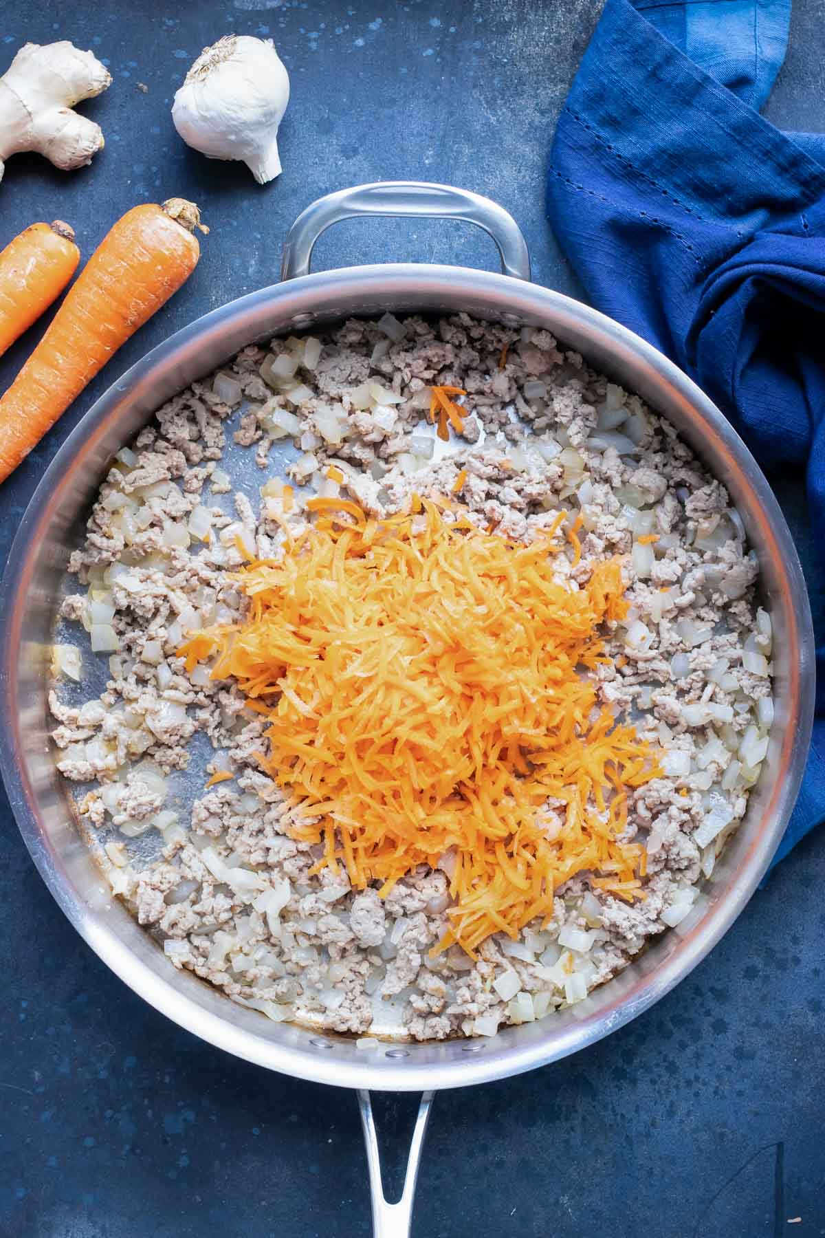 Adding shredded carrots to a large skillet.