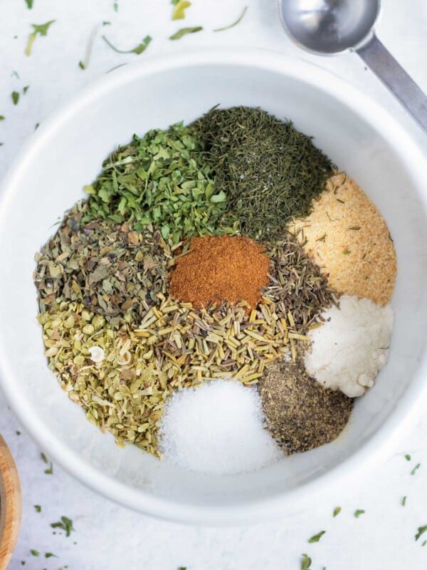Spices and herbs are in a white bowl for a Greek seasoning recipe.