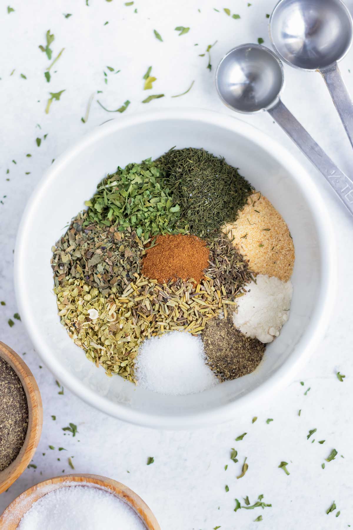 Spices and herbs are in a white bowl for a Greek seasoning recipe.