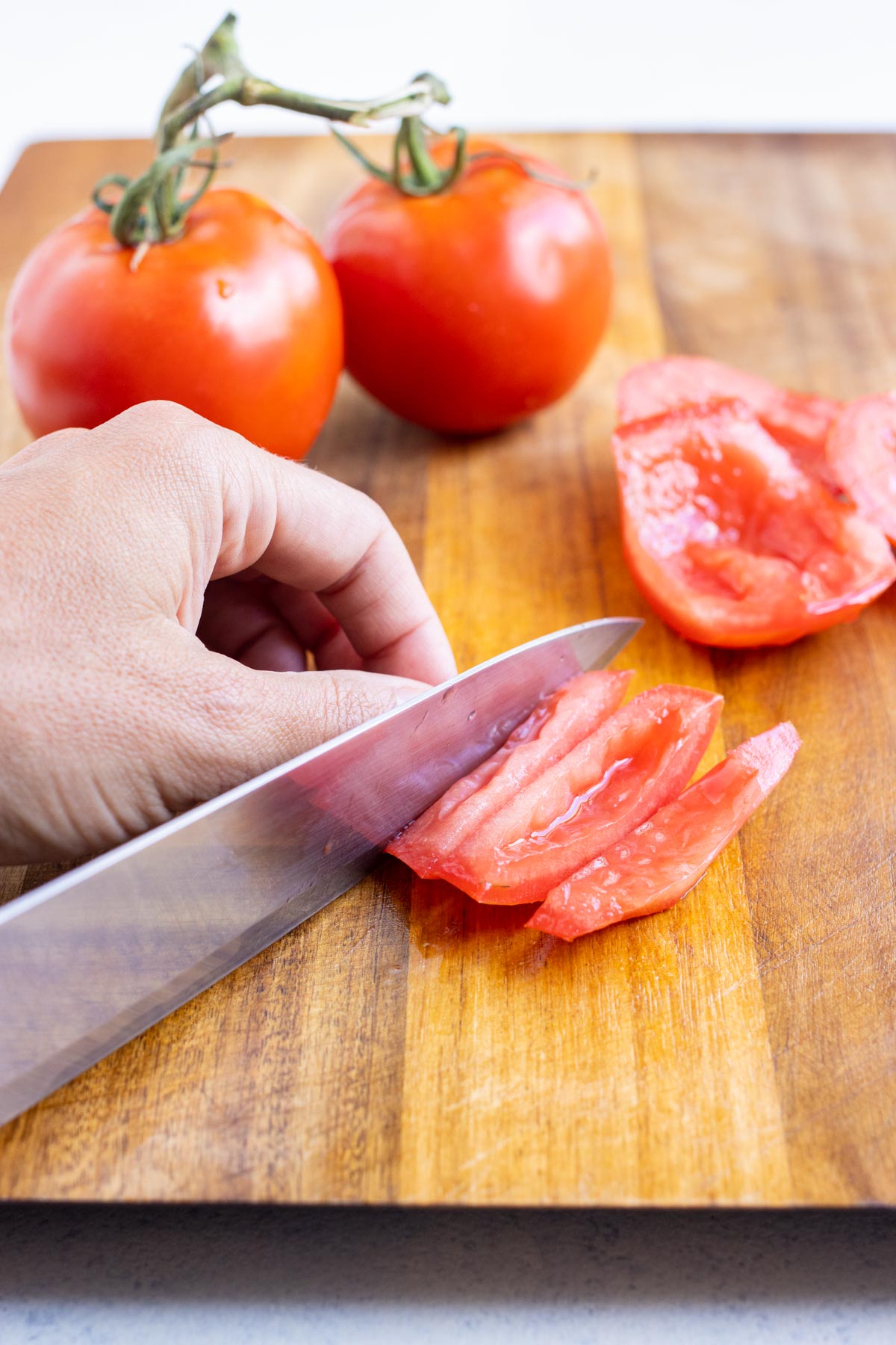 A knife cuts a tomato wedge into small slices.