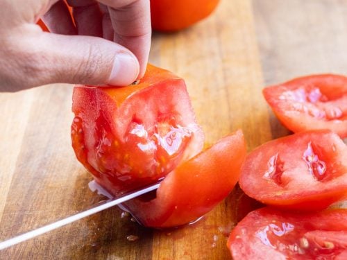 A knife cuts wedges away from the core of a tomato.