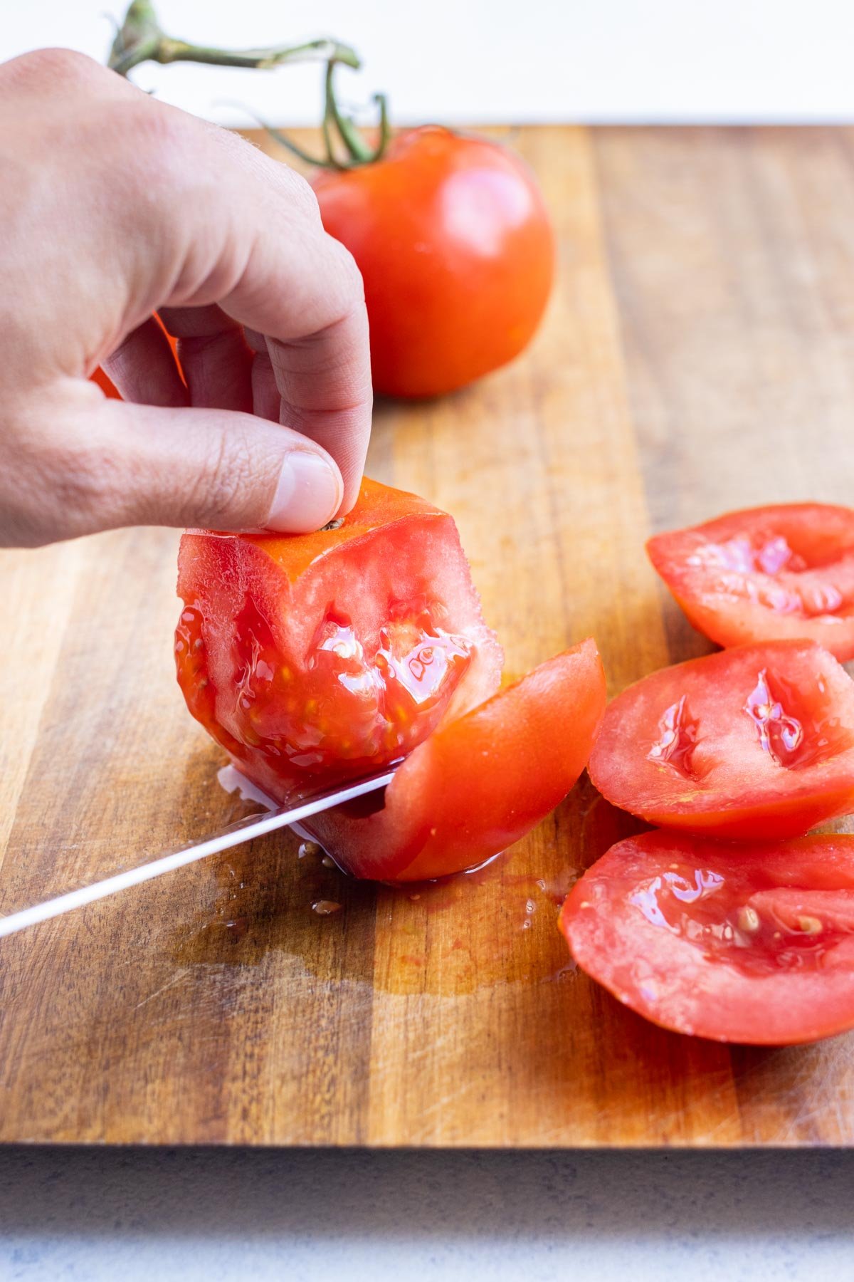 A knife cuts wedges away from the core of a tomato.