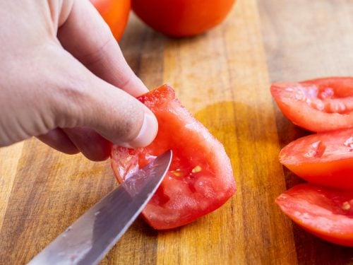 A knife carefully removes the seeds from the tomato flesh.