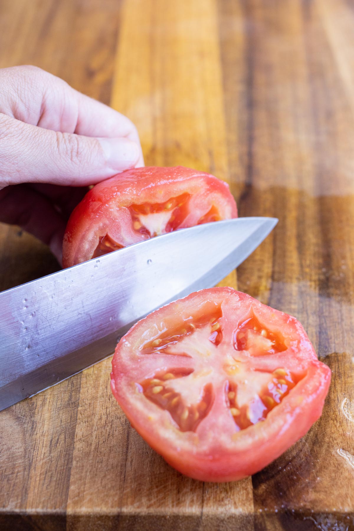 A sharp knife slices a peeled tomato in half to remove the seeds.