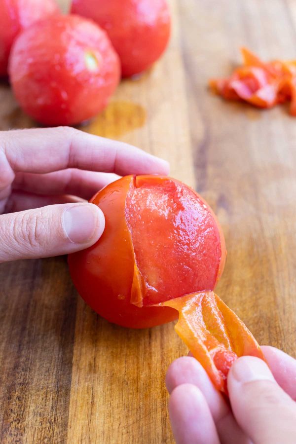 A hand pulls the skin off a tomato