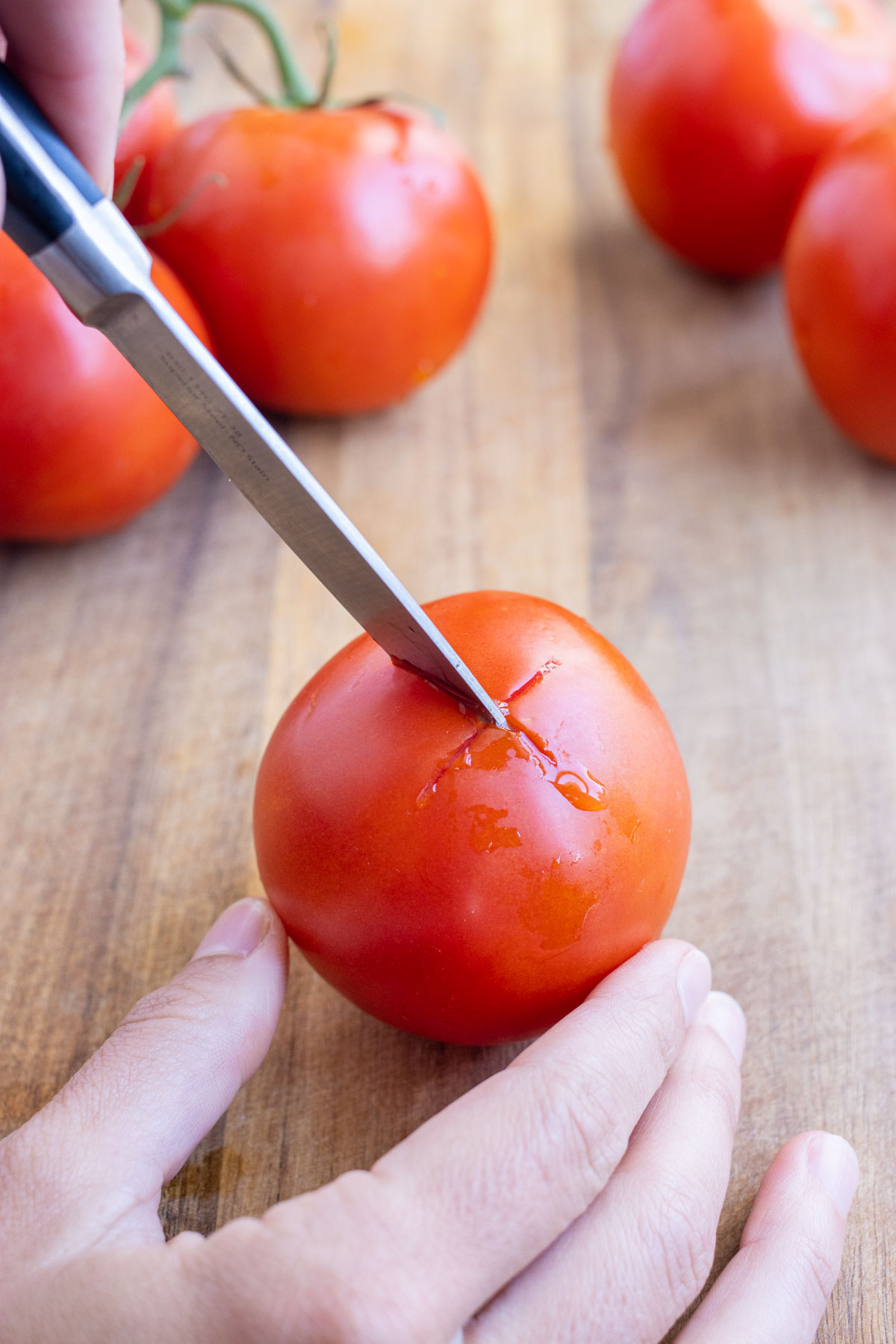 A sharp knife scores an X on the bottom of the tomato to make peeling easier.