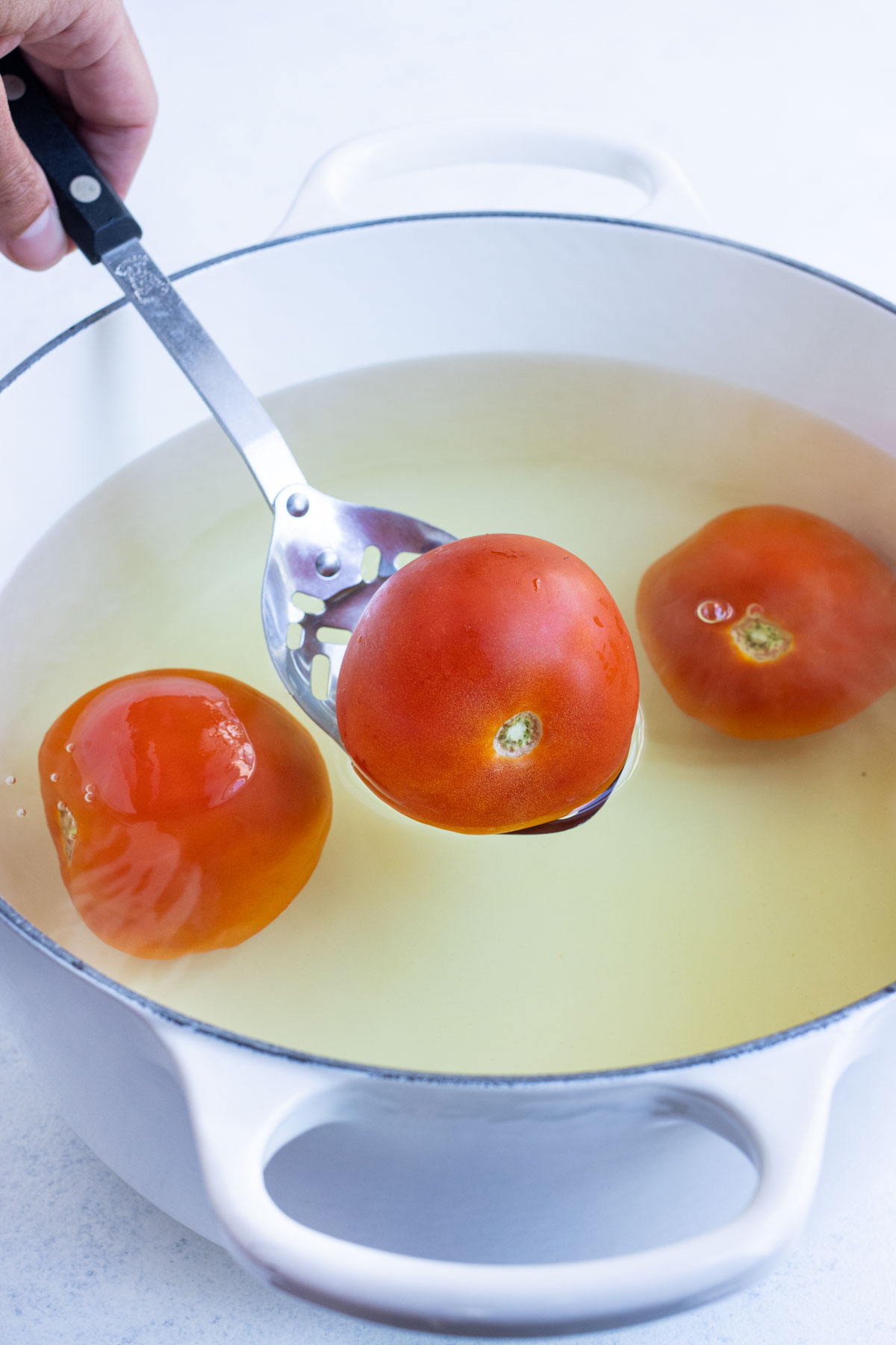 A slotted spoon lifts tomatoes out of boiling water.