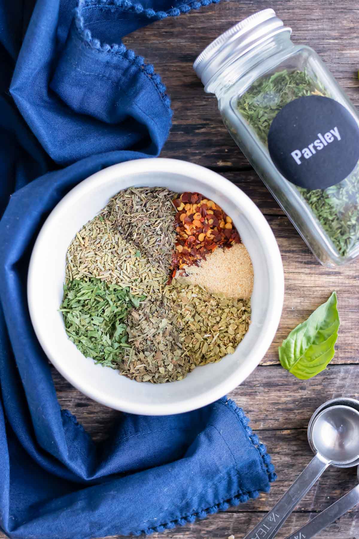 Homemade Italian seasoning in a white bowl next to a jar of dried parsley.