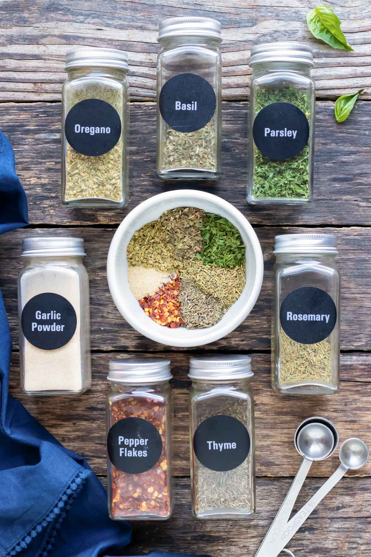 Dried oregano, basil, parsley, rosemary, thyme, garlic powder, and red pepper flakes in jars showing how to make a homemade Italian seasoning recipe.