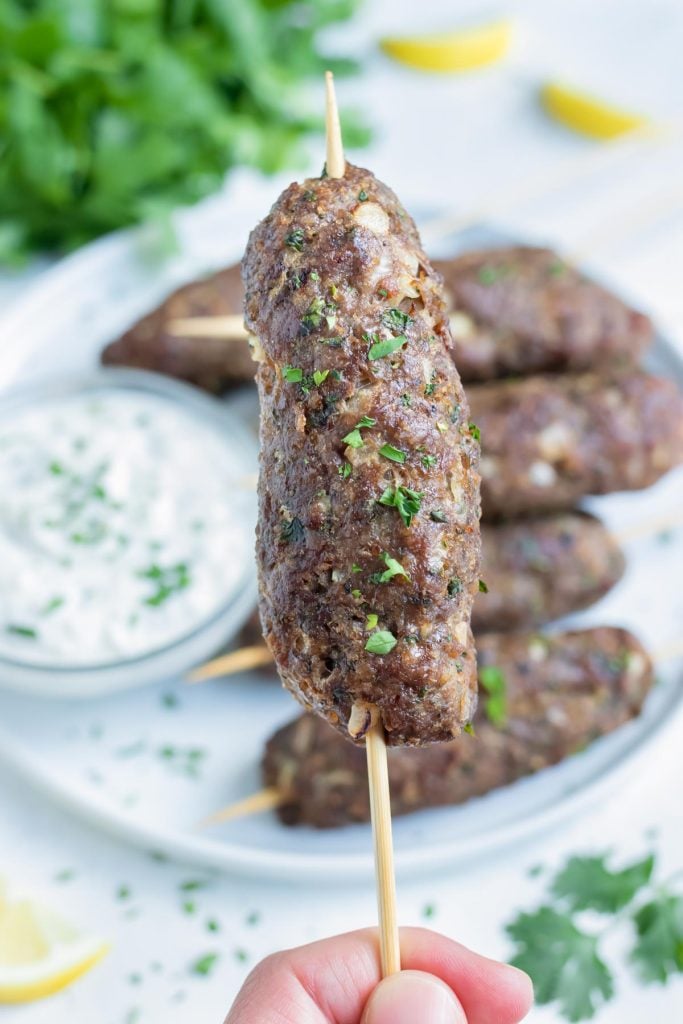 A hand is used to hold up one lamb kebab.