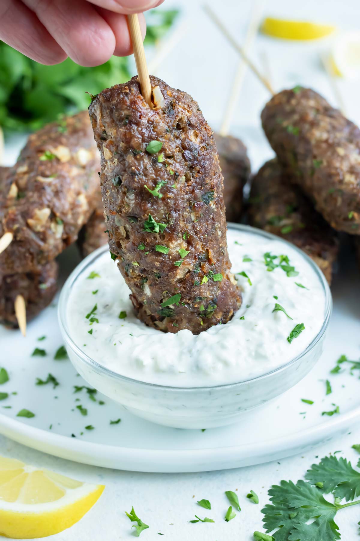 A hand is used to dip gluten-free Lamb Kofta into Tzaztiki sauce.