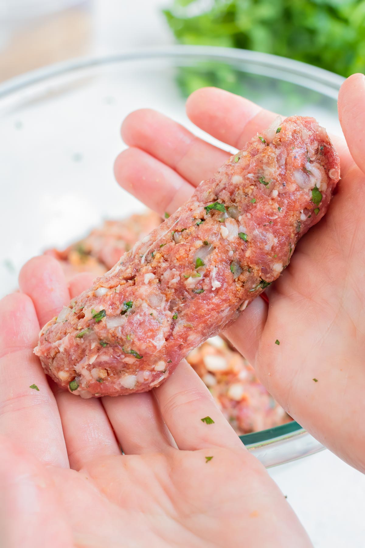 A hand is used to mold the lamb kofta into kebabs.