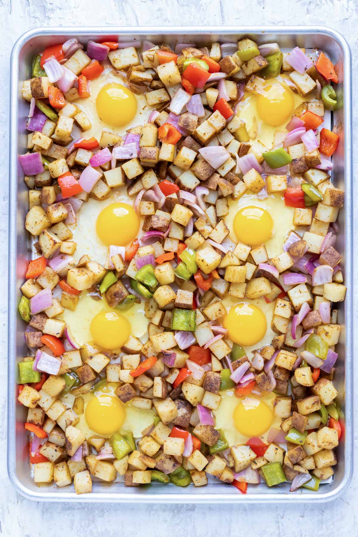 8 eggs are cracked into the wells formed in chopped veggies.