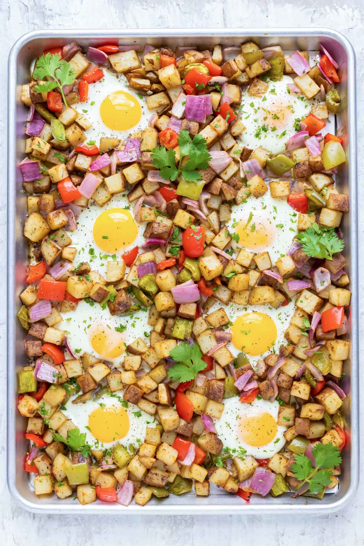 A sheet pan full of a breakfast potato hash and eggs with cilantro sprinkled on top.