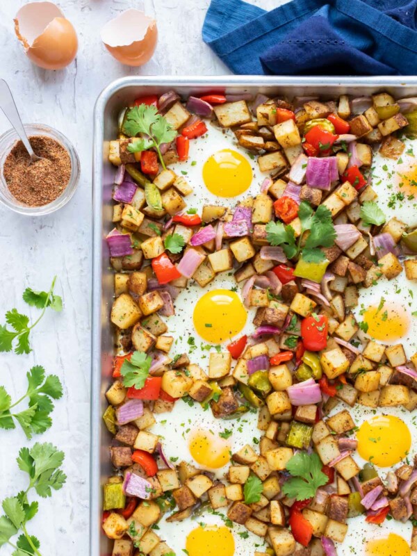 A sheet pan full of a breakfast potato hash recipe with over-easy eggs and blackened seasoning.