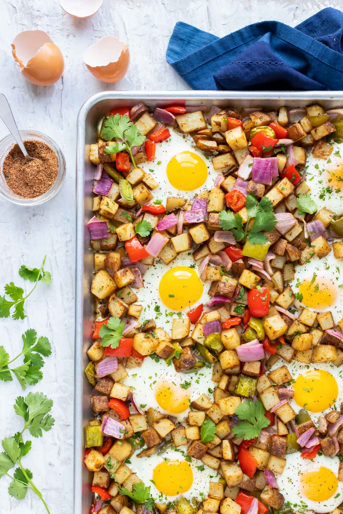 A sheet pan full of a breakfast potato hash recipe with over-easy eggs and blackened seasoning.