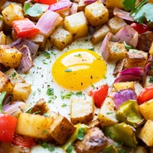 Three eggs surrounded by oven-roasted breakfast hash with red bell pepper and red onion.