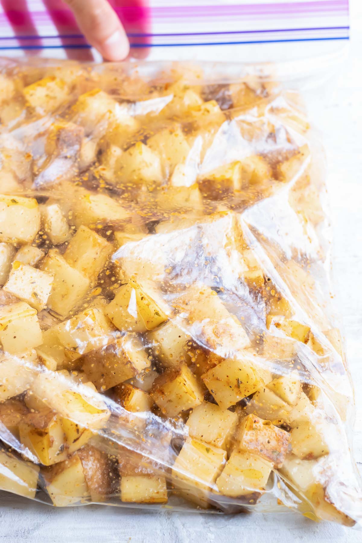 A bag is full of chopped and seasoned potatoes.