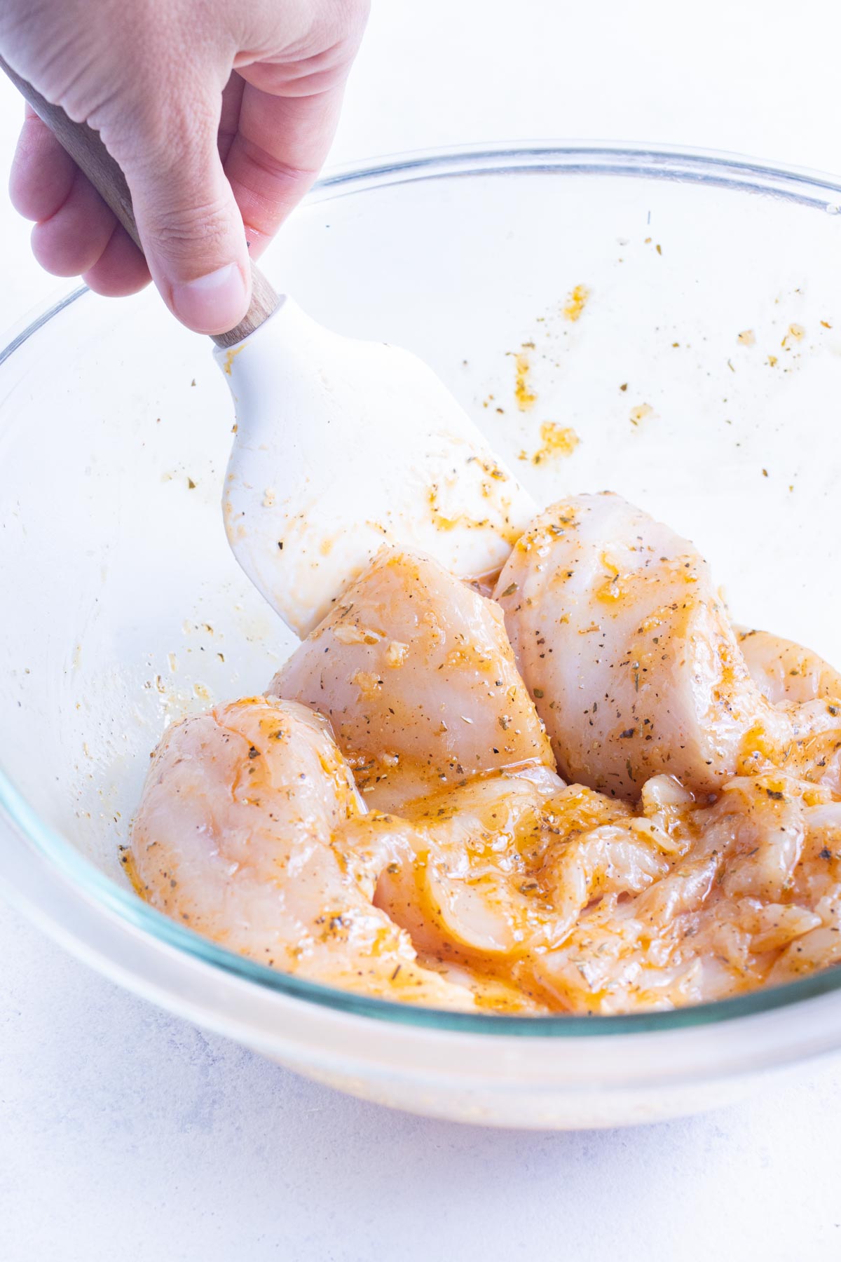 Chicken is tossed with a marinade in a glass bowl.