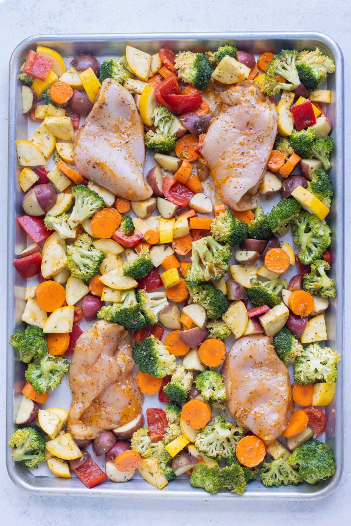 Raw chicken and veggies are seasoned and ready to bake.