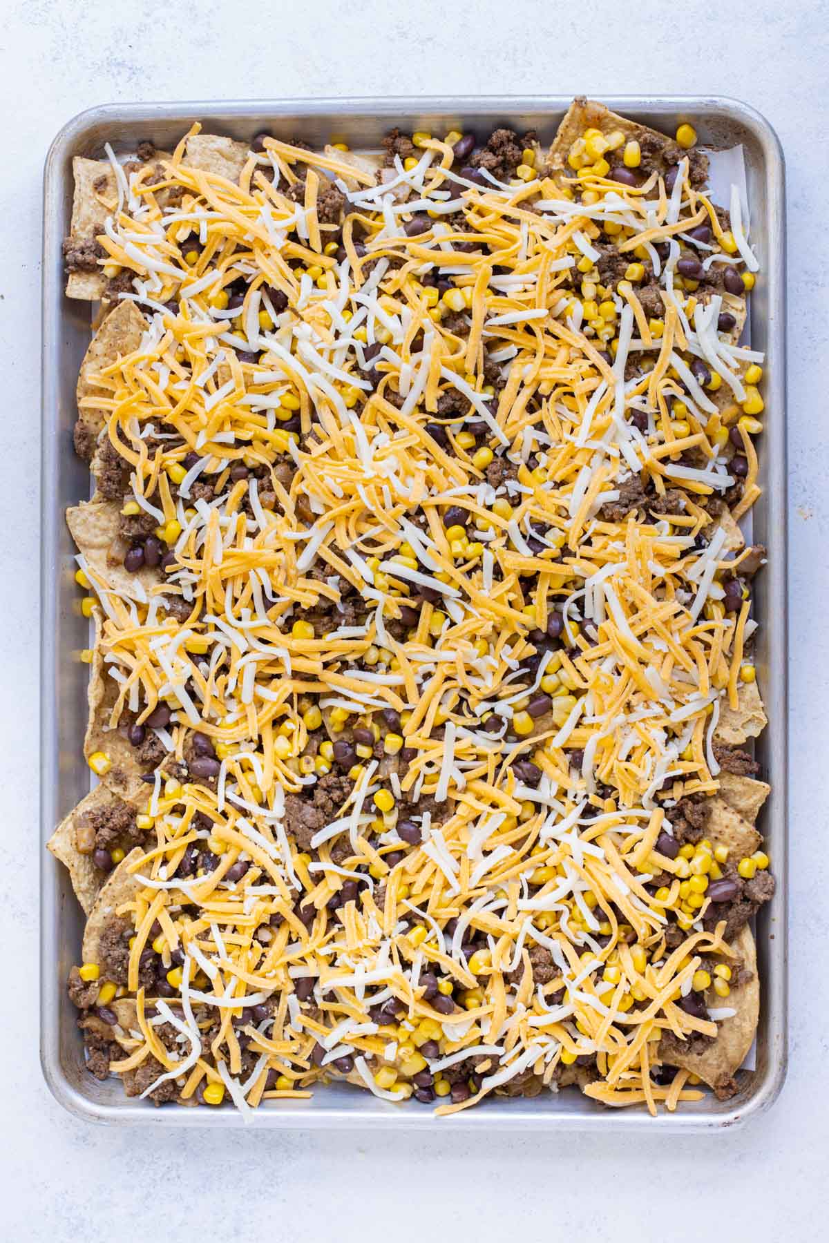 Cheese is sprinkled over the chips, beef, beans, and corn.