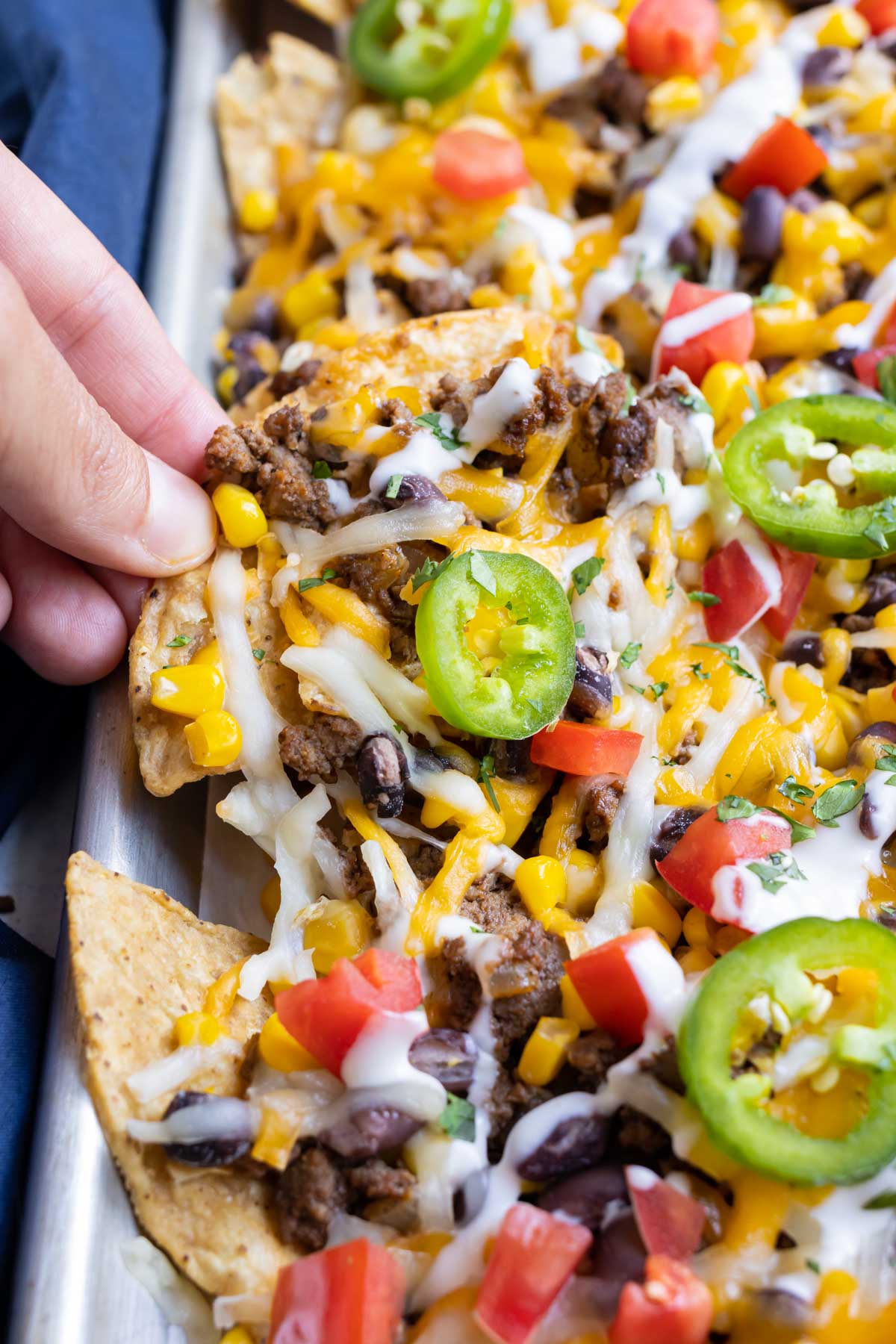 A hand picks up a serving of nachos from the sheet pan.