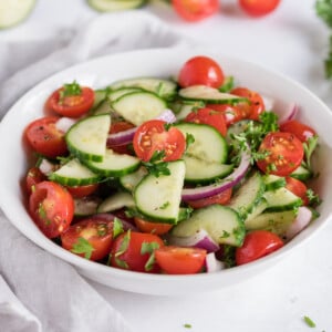 Cucumber tomato salad in a white bowl.