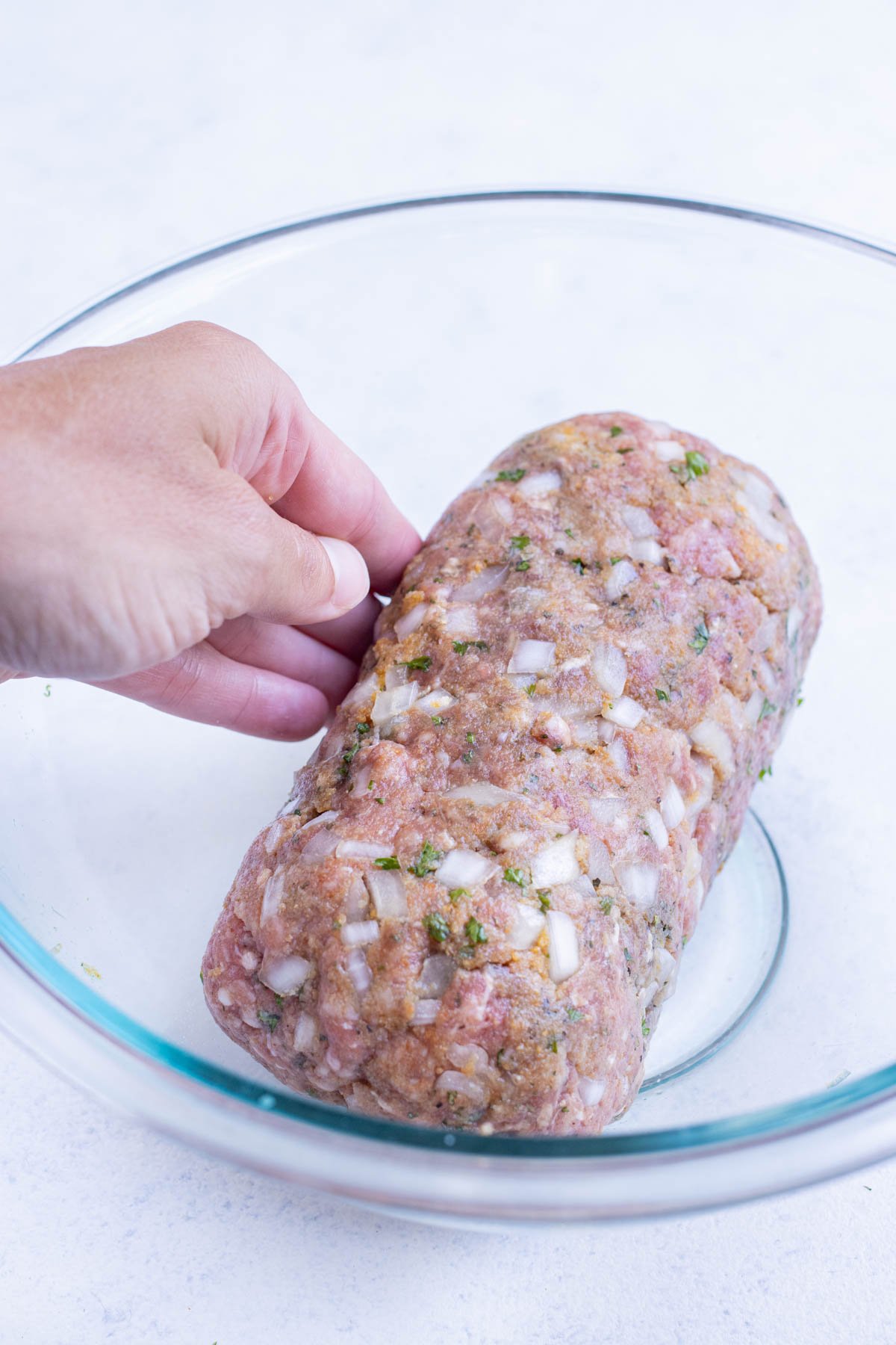 Hands shape the meatloaf mixture into a log.