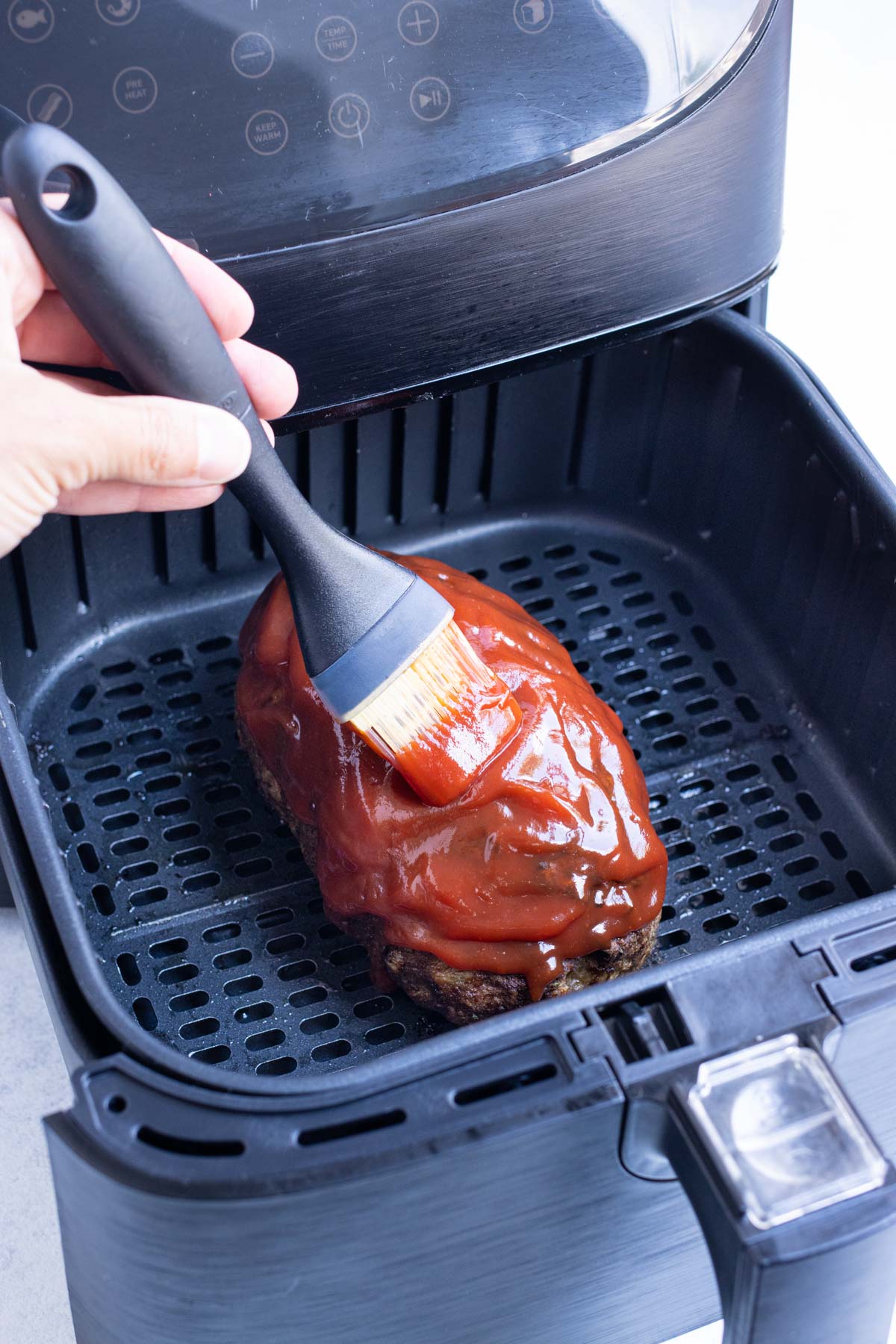 Glaze is brushed onto meatloaf in the air fryer.