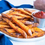A plate of sweet potato fries are served at a meal with ketchup.
