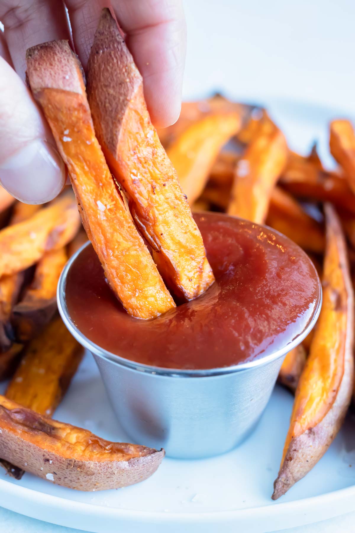 Two sweet potato fries are dipped into ketchup.