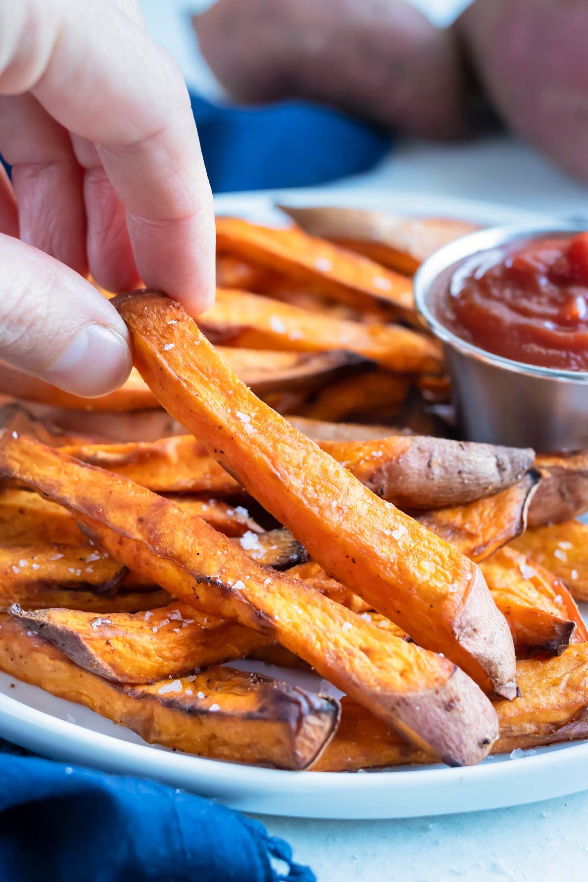 A sweet potato fry is lifted up by a hand for a healthy side.