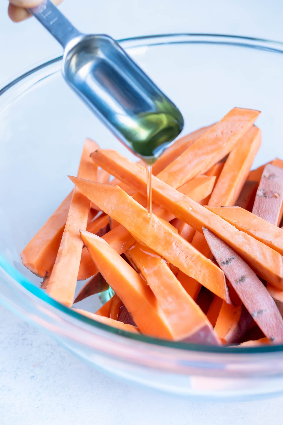 Avocado oil is poured onto the raw sweet potato fries.