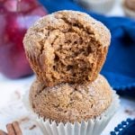 A fluffy and healthy applesauce muffin sits on top of another one in a stack with a bite taken out of it.