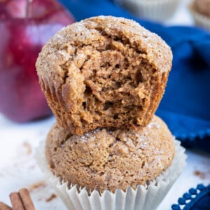 A fluffy and healthy applesauce muffin sits on top of another one in a stack with a bite taken out of it.