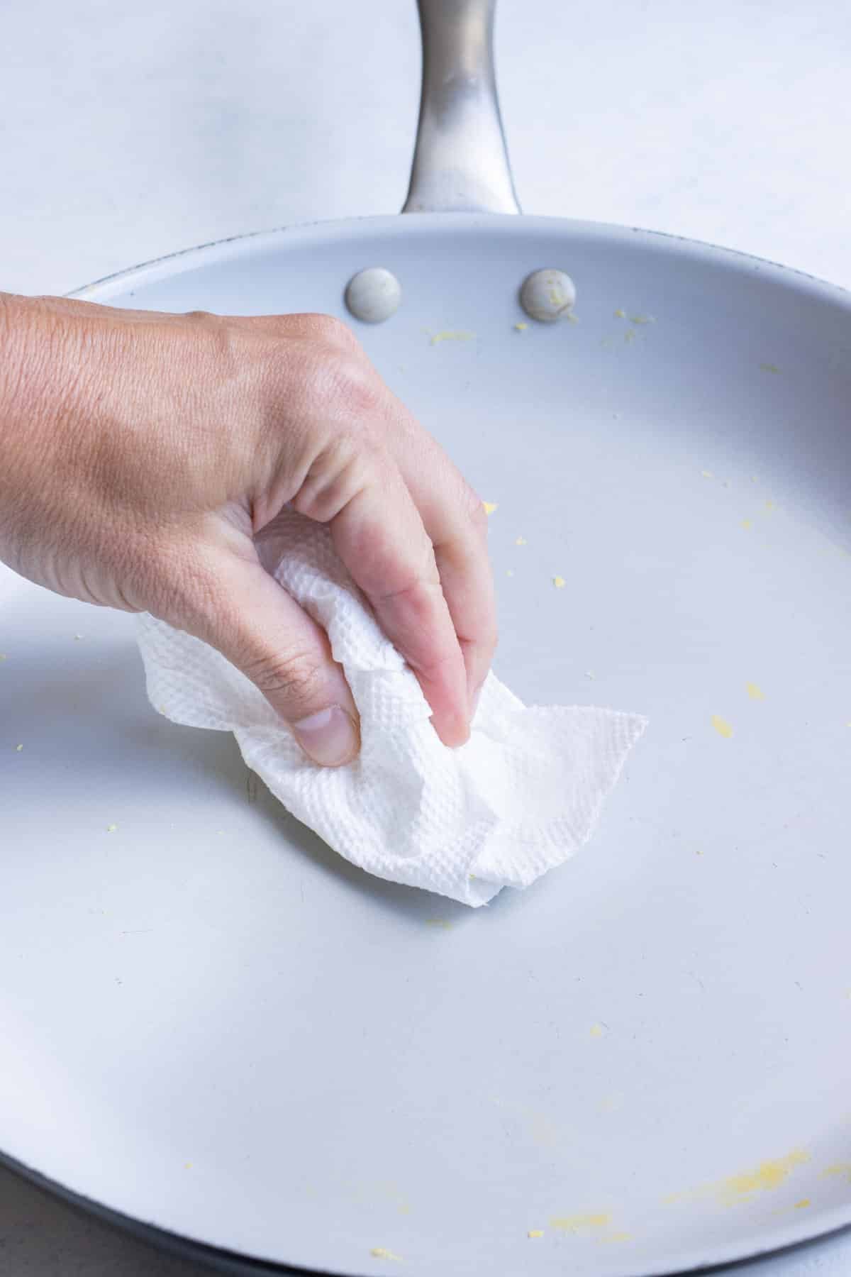 A hand wipes down the skillet after scrambling eggs.