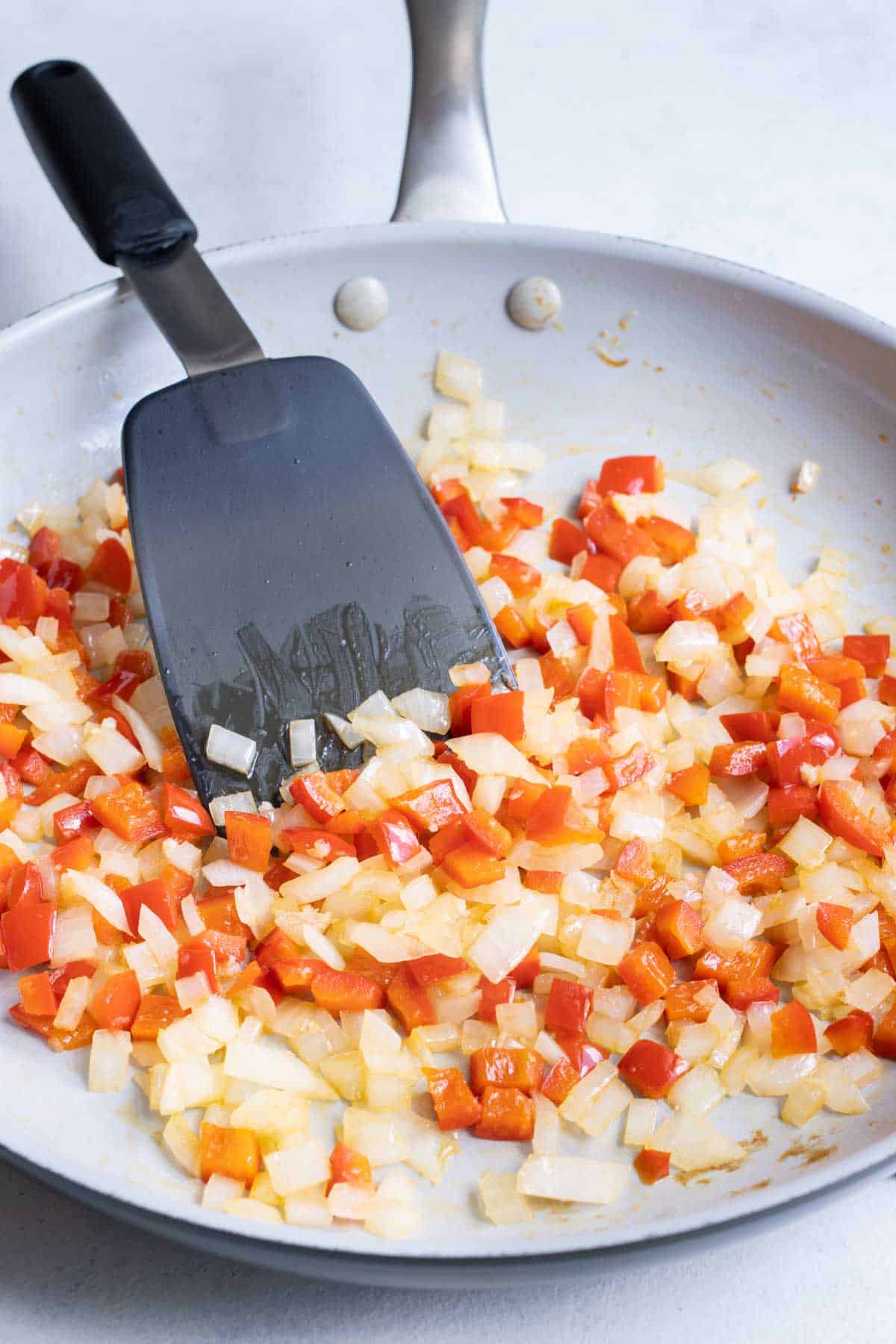 Onions and bell pepper are cooked in a skillet.