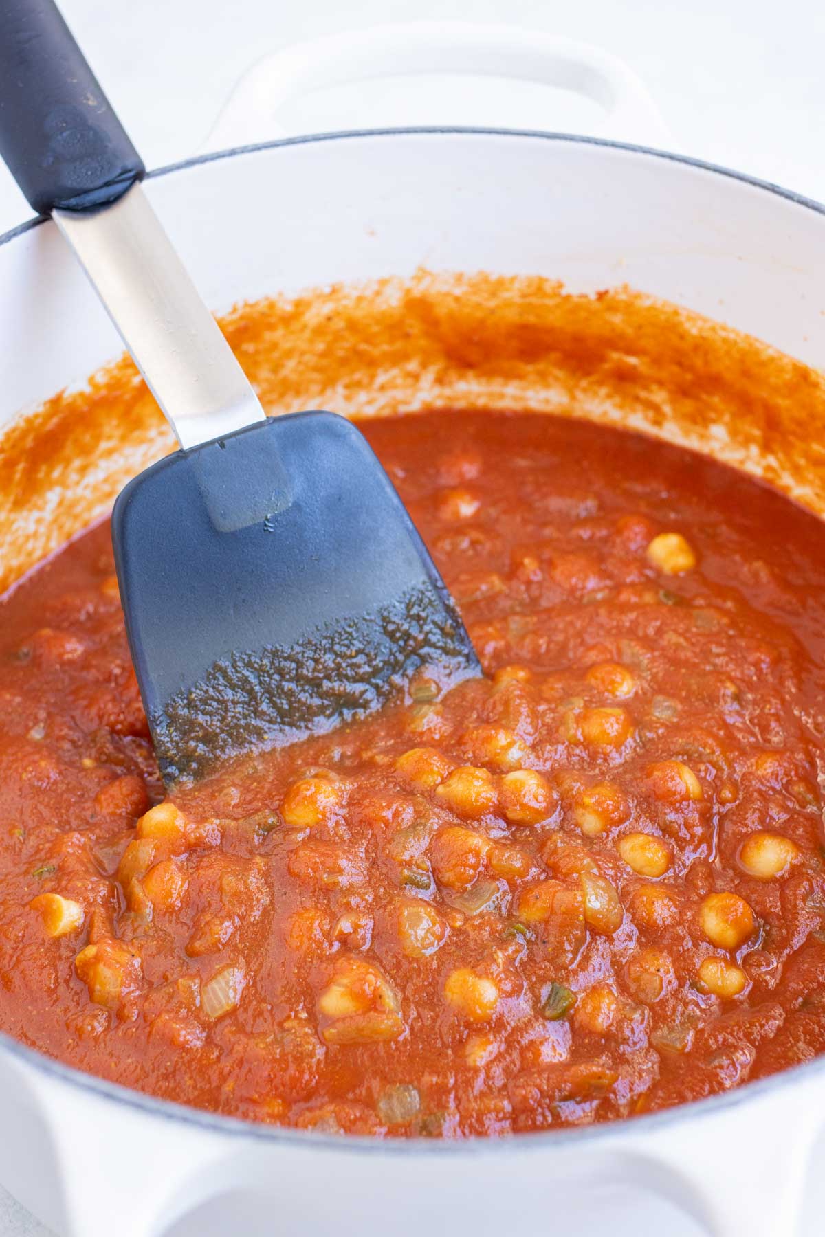 A spatula stirs chana masala after tomatoes and chickpeas are added.