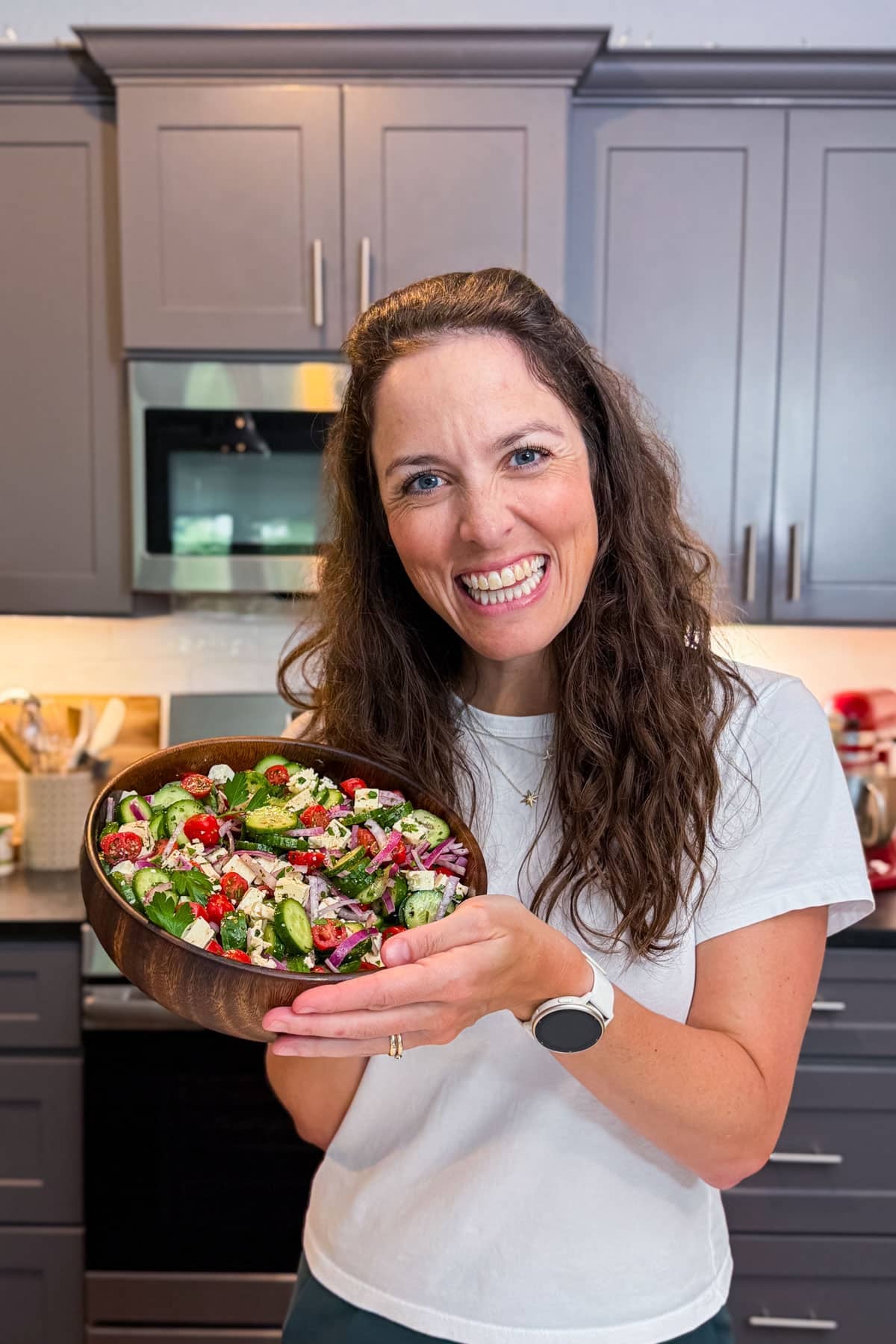 London Lea holding a bowl of a Greek cucumber tomato and feta salad in her Austin, Texas kitchen.