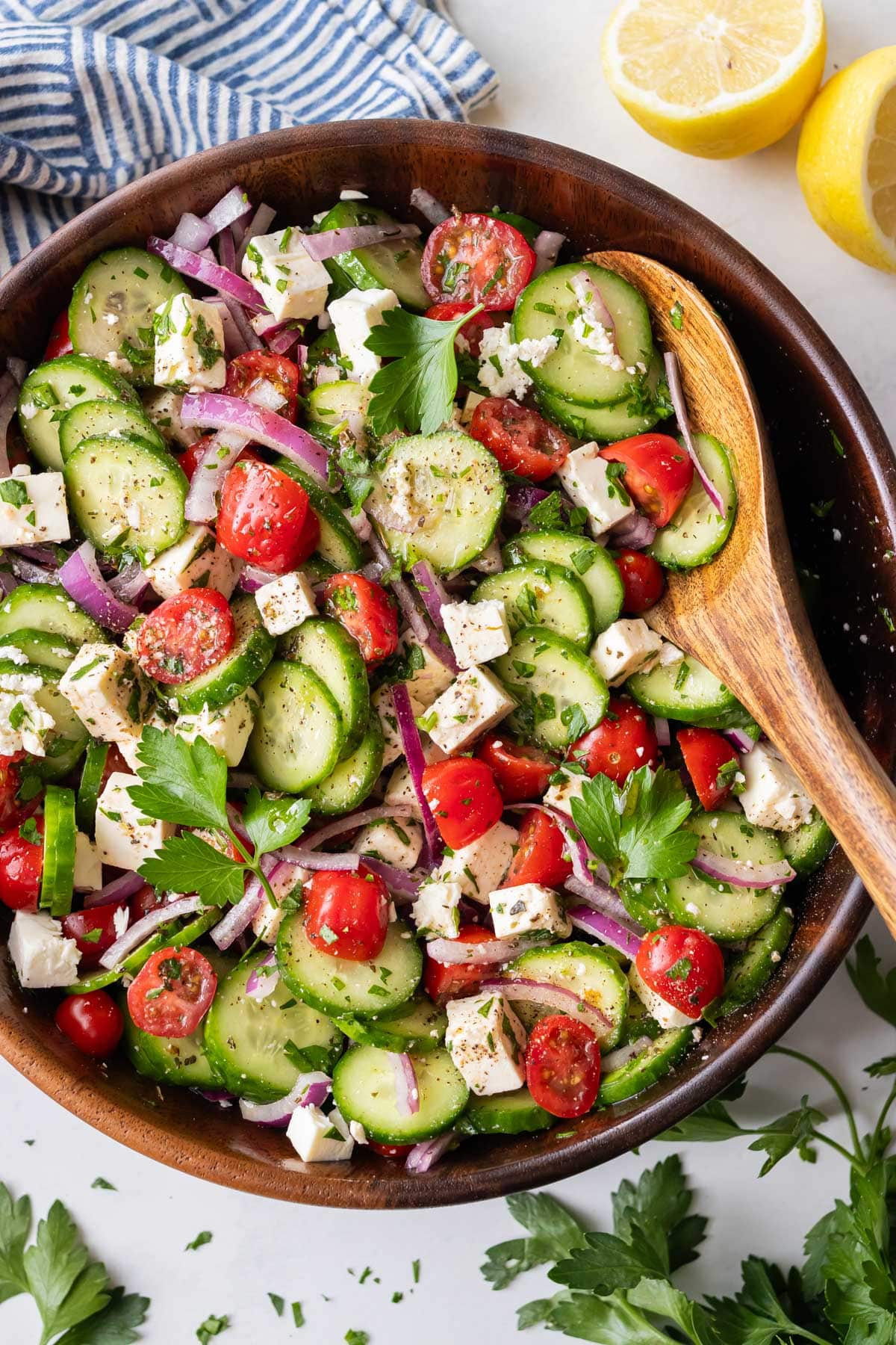 A Greek cucumber tomato and feta salad is served in a wooden bowl for a simple summer side dish.
