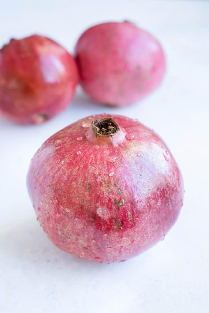 A whole pomegranate is on a table with two more in the background.