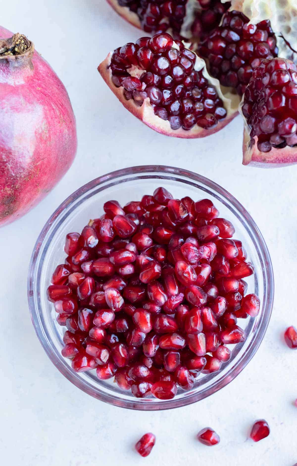 Pomegranate seeds are placed in a bowl near a cut open pomegranate.
